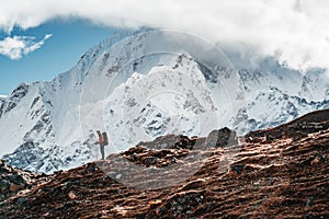 Solo tourist with travel backpack stand in front of snowy and cloudy mountains. Traveler among high altitude mountain