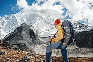 Solo tourist with travel backpack stand in front of snowy and cloudy mountains. Traveler among high altitude mountain