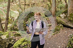 Solo tourist Woman with paper map and smartphone hiking on footpath in spring forest. Person in sport clothes walking on