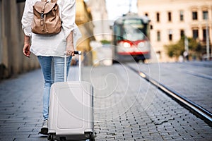 Solo traveler. Woman tourist with backpack pulling suitcase and walking on street