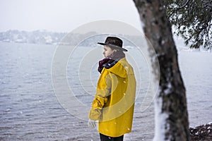 Solo traveler with yellow rain coat and cowbow hat lookng away under snow, back shot