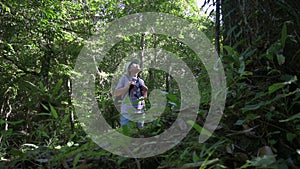 Solo woman hiker with backpack stop to see the directions under a big tree while walking in the forest park.