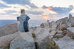 Solo young female traveler watches a beautiful sunset on spectacular rocks of Capo Testa, Sardinia, Italy.