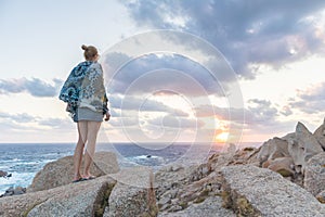 Solo young female traveler watches a beautiful sunset on spectacular rocks of Capo Testa, Sardinia, Italy.
