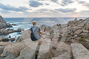 Solo young female traveler watches a beautiful sunset on spectacular rocks of Capo Testa, Sardinia, Italy.