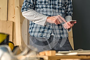 Solopreneur carpenter using smartphone in small business woodwork workshop