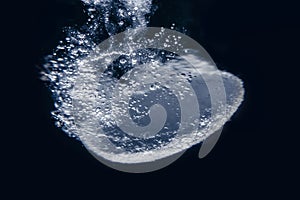 A soluble tablet dropped in a glass of water over dark background