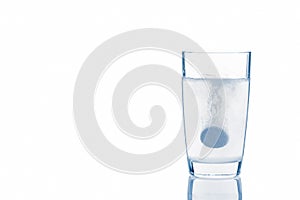 A soluble tablet dropped in a glass of water over white background