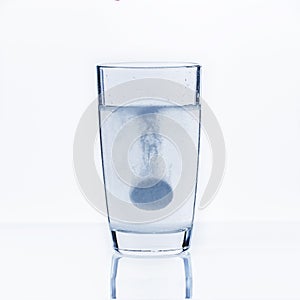 A soluble tablet dropped in a glass of water over white background