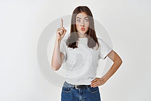 Solution. Young trendy woman having an idea, pointing finger up and pucker lips excited, suggesting plan, standing over