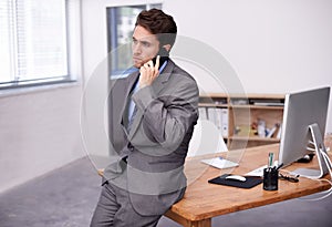 Solving business problems via cellphone. A young businessman busy on an important call in his office.