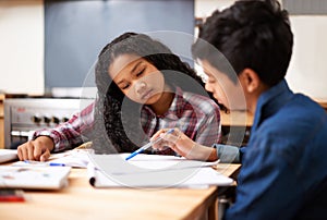 Solving their homework together. Shot of two young students studying together in a classroom.