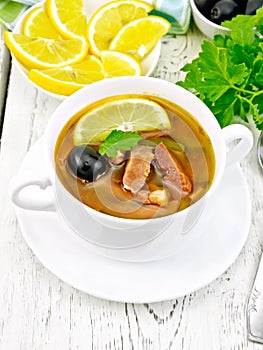 Solyanka with lemon in white bowl on light board