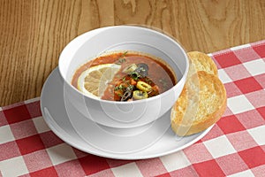 Solyanka, Russian soup with meat, olives and sour cream. served in a white bowl over red plaid tablecloth