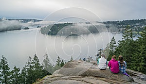 some children sitting on a rock with water behind them and trees in the foreground