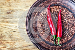 Some chili peppers on dark plate, fresh red ripe hot chilli on old wood board background with copy space, guinea pepper or bird pe