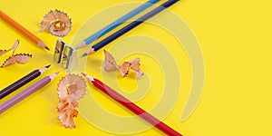 Some colored pencils of different colors and a pencil sharpener and pencil shavings on Ð° yellow background