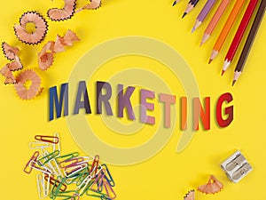 Some colored pencils of different colors and a pencil sharpener and pencil shavings on the yellow background. Word MARKETING