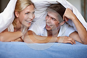 Some days are just meant for playing. a happy young couple enjoying a playful moment underneath the duvet.