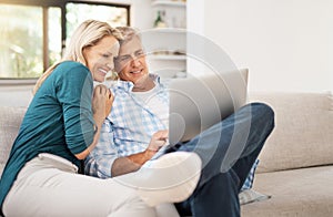 Some downtime. an affectionate mature couple using a laptop while sitting on the sofa together at home.