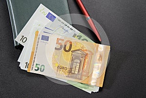 Some Euro banknotes with pen and notepad on dark