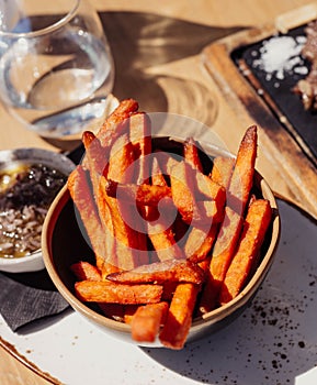 French fries served in a bowl on a wooden table. Sweet potatoes