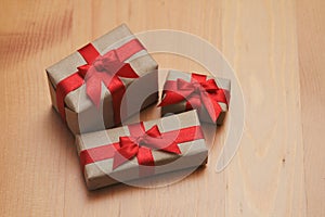Some gift boxes wrapped in brown craft paper and tie red satin ribbon. Decorative wooden background. Your text space.