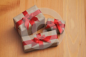 Some gift boxes wrapped in brown craft paper and tie red satin ribbon. Decorative wooden background. Your text space.