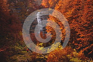 Some hikers in front of the Morricana Waterfalls in Monti della Laga, Abruzzo, Italy, in the full autumn season with red and