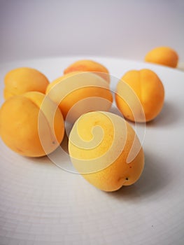 Some juicy ripe sweet apricots lie on a large round white plate that stands on a wooden table.