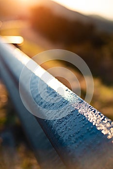 Some moist cold morning dew on a blue metal bench while yellow sunrise light and heats it up