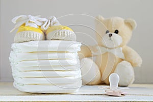 Some nappies on a white wooden table. Sneakers, a pacifier and a teddy bear. photo