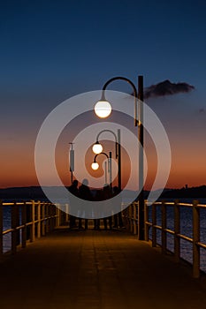 Some people on a pier at Trasimeno lake Umbria, Italy at dusk, with beautiful water reflections and warm colors