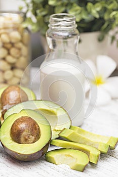 Some pieces of sliced avocado on the table and a bottle of milk and maccadamia