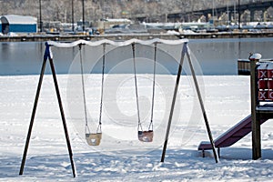 Some playground swings covered in snow .