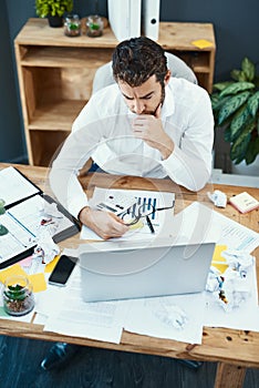 Some problems take longer to tackle. a young businessman looking serious while working on a laptop in an office.