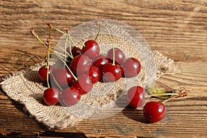 Some ripe red juicy cherries on sackcloth on an old wooden rustic bench. Harvesting. Bright sunlight.