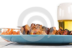 Some shashlik spits on a bluish plate, decorated with a beer in