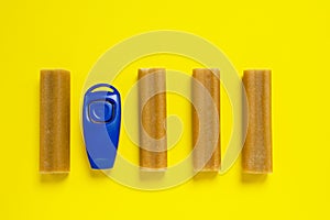 Some sticks of dog delicacy and clicker, special training appliance, on bright yellow background