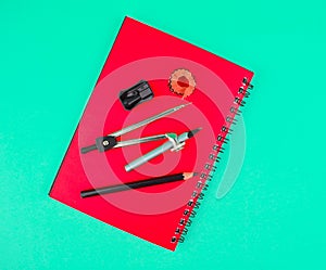 Some study material containing a pencil compass,a pencil sharpener a crayon on top of a red diary