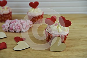 Some Valentines day romantic cup cakes with red love heart decorations on top and pink paper roses