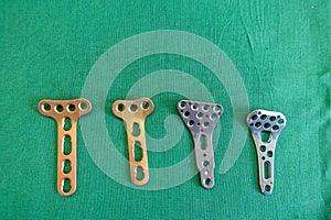 Some various explanted radius plates lie spread out on a green surgical drape