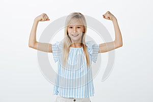 Someday girl become famous sportswoman. Little confident kid with blond hair in blue blouse, raising hands with clenches