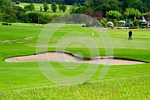 Someone golfing behnd a sandpit of a golf course