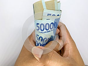 someone hands holding a roll of money of 50000 indonesian banknotes. Rupiah is Indonesian currency. Isolated on white background