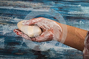 Someone is holding a piece of toilet soap on a wooden background in a soapy hand. Close up. Frequent hand washing with soap is a