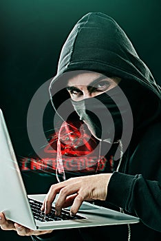 Someone is in for a nasty surprise. Portrait of a computer hacker using a laptop while standing against a dark