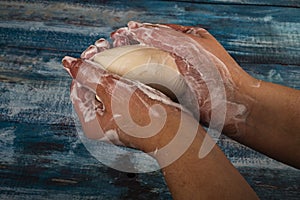 Someone is soaping their hands with a piece of toilet soap on a wooden background. Close up. Frequent hand washing with soap is a