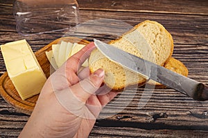 Someone spreads butter with a knife on fresh wheat toast, butter and cheese in a wooden butter dish on a wooden background. Close