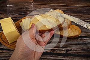 Someone spreads a little butter on fresh wheat toast with a knife and a wooden butter dish with a piece of butter on a wooden